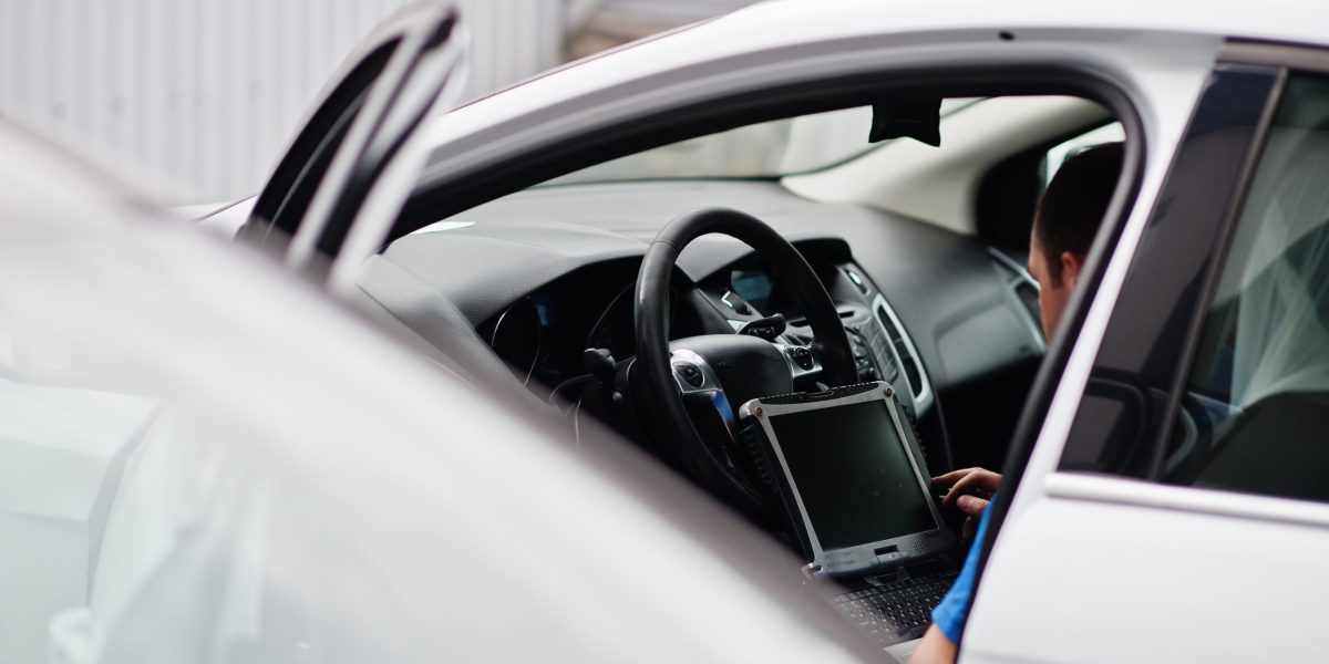 Car repair and maintenance theme. Electric mechanic in uniform working in auto service, making car diagnostics using obd device with laptop.